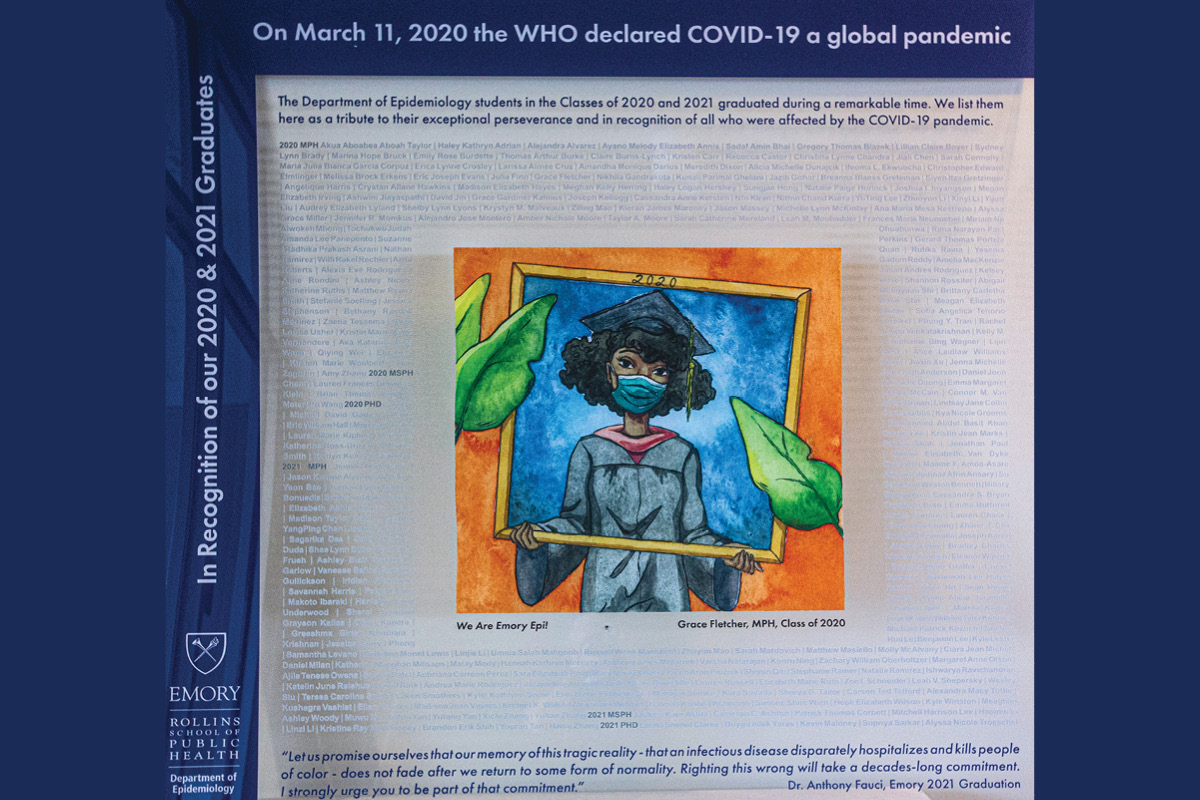 A photo of a piece of art depicting a woman in cap and gown wearing a mask being viewed through a computer monitor screen which she is holding