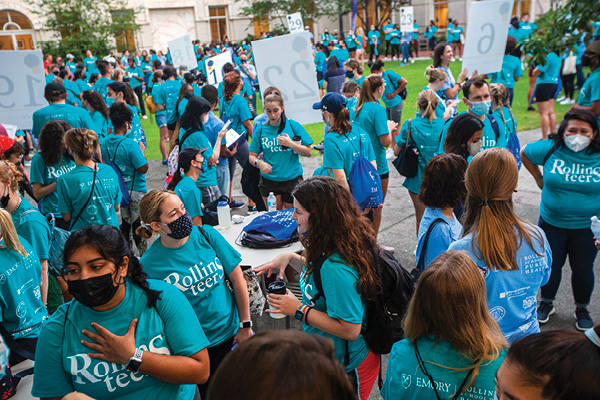 Rollins students in teal Rollins t-shirts stand outside in a large group while wearing masks