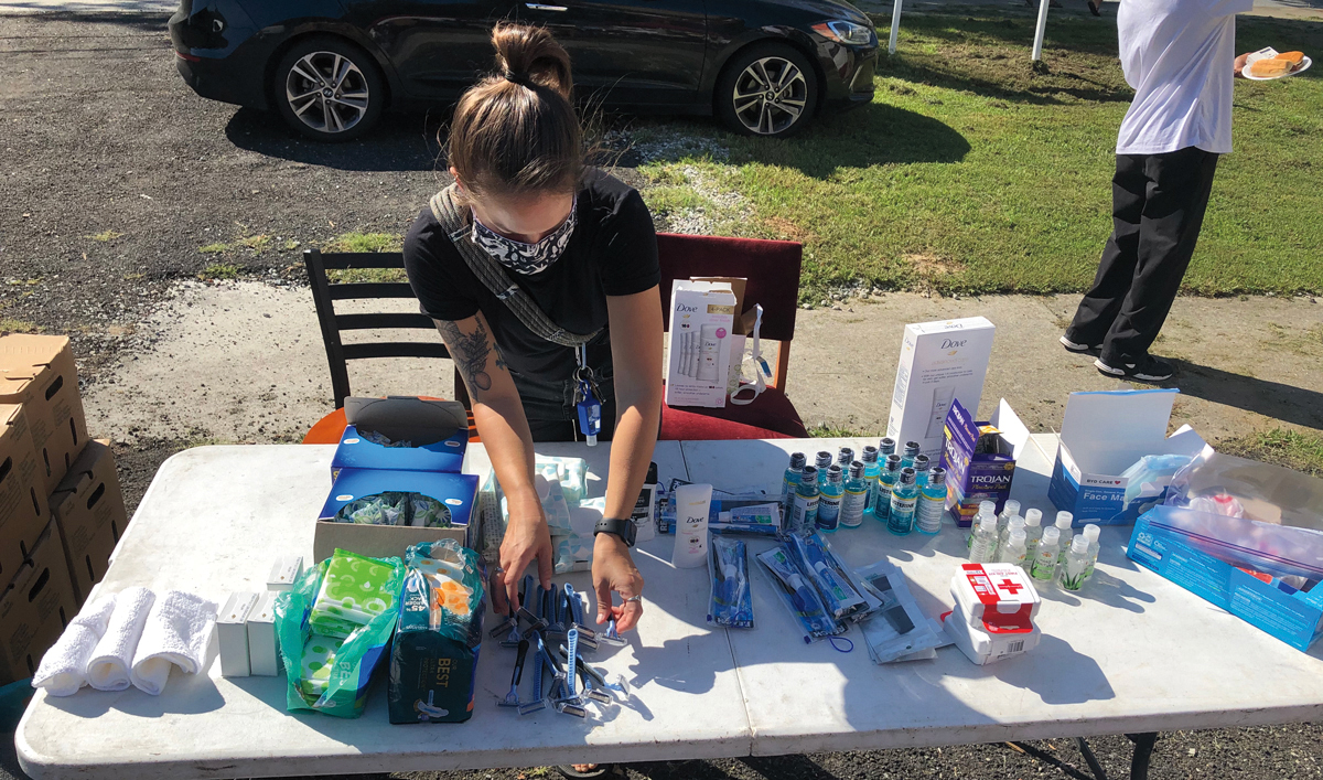 A masked volunteer arranges personal care items for the homeless on a table.