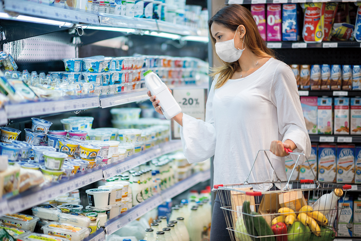 A masked woman shops in the dairy aisle of a grocery store