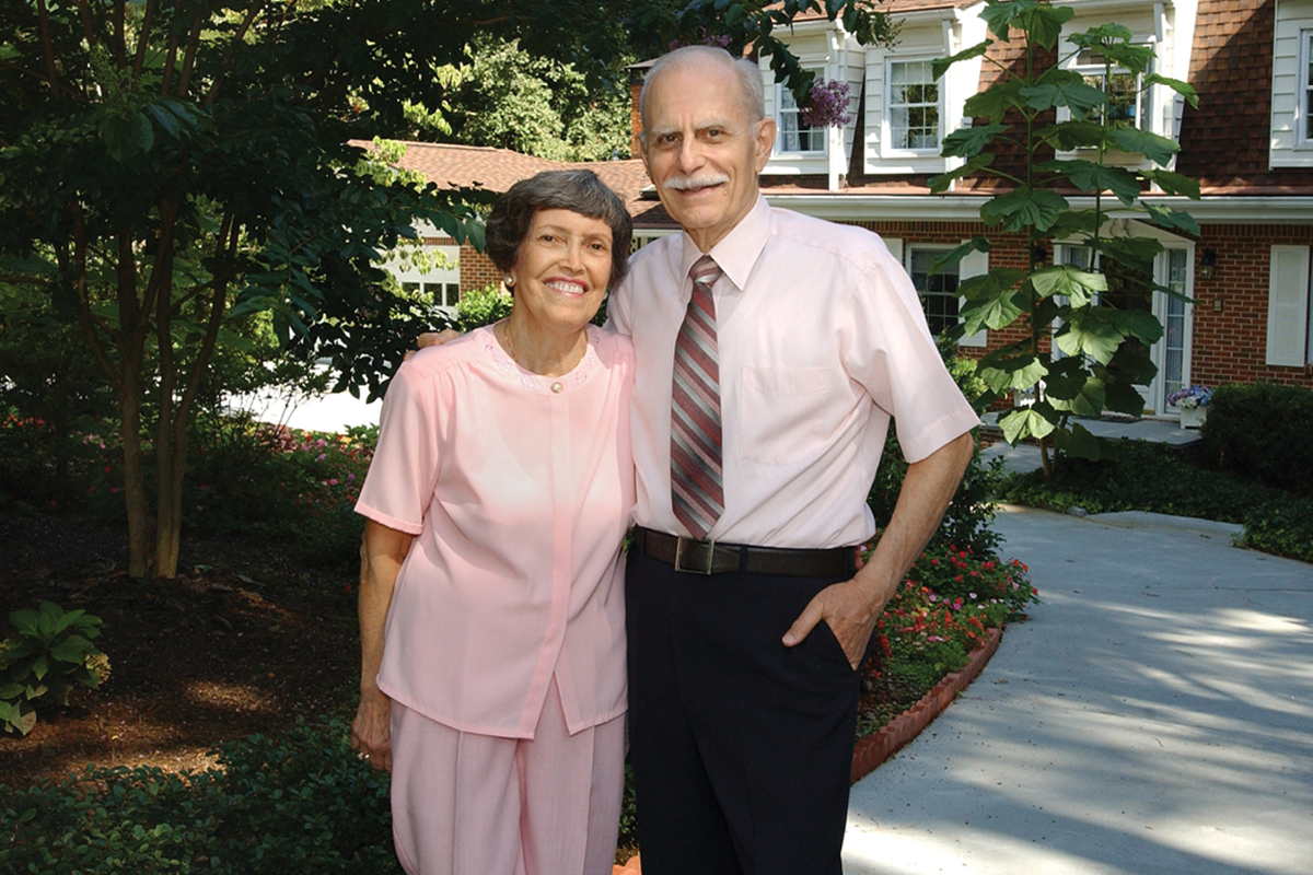 an elder couple standing in front of the house hugging and smiling.