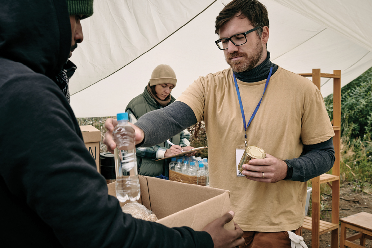 a stock photo of a volunteer passing out bottle waters to the homeless