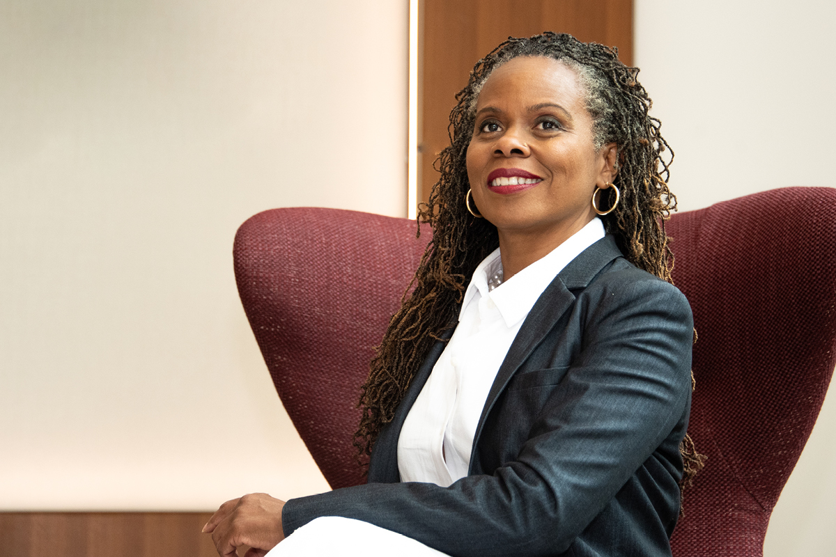 a black woman sitting in a maroon chair and smiling to the camera.